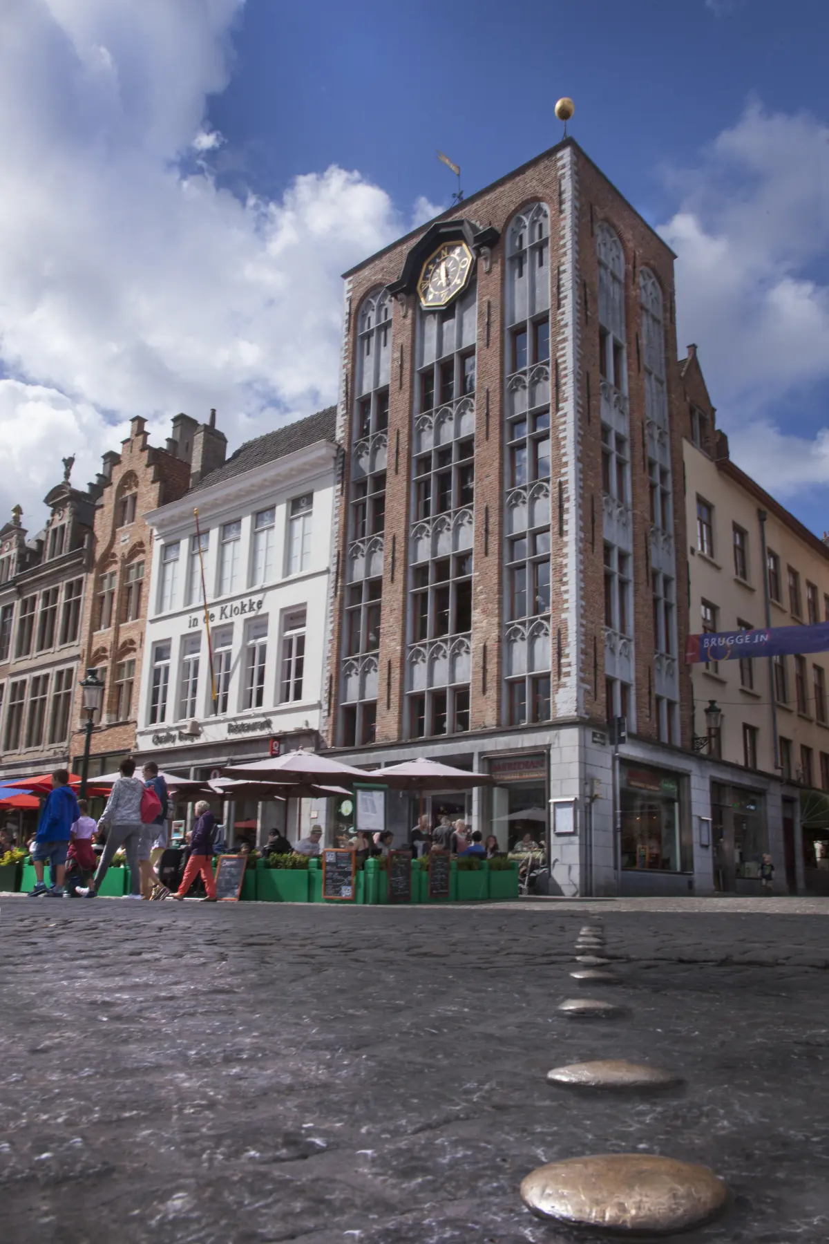 'Front and side facade of the corner house, with the golden sphere on top of the building's corner. Copper nails are lying on the ground of the Markt.