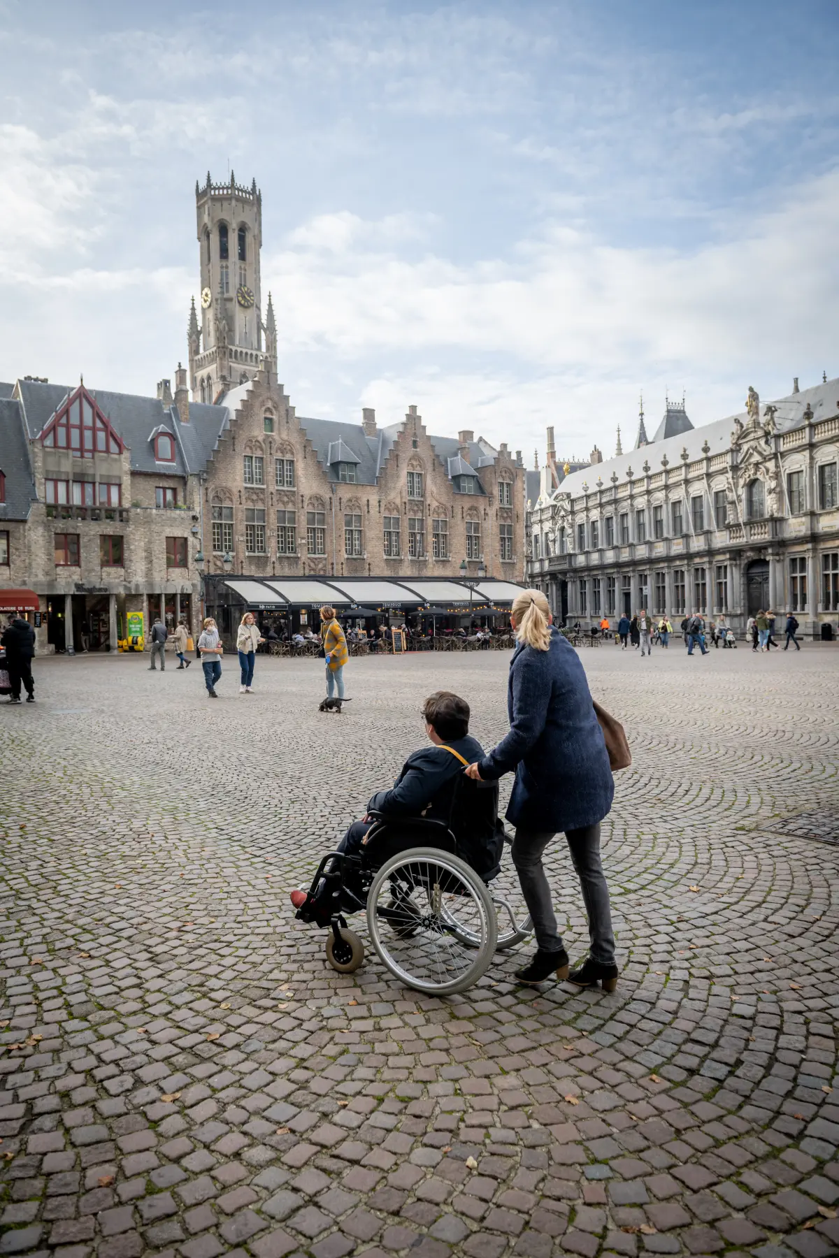 wheelchair user with assistant on the Burg, in the background, the Belfry is visible