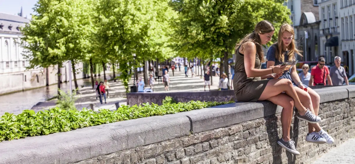 two women sitting on a wall, the Dijver out of focus in the background