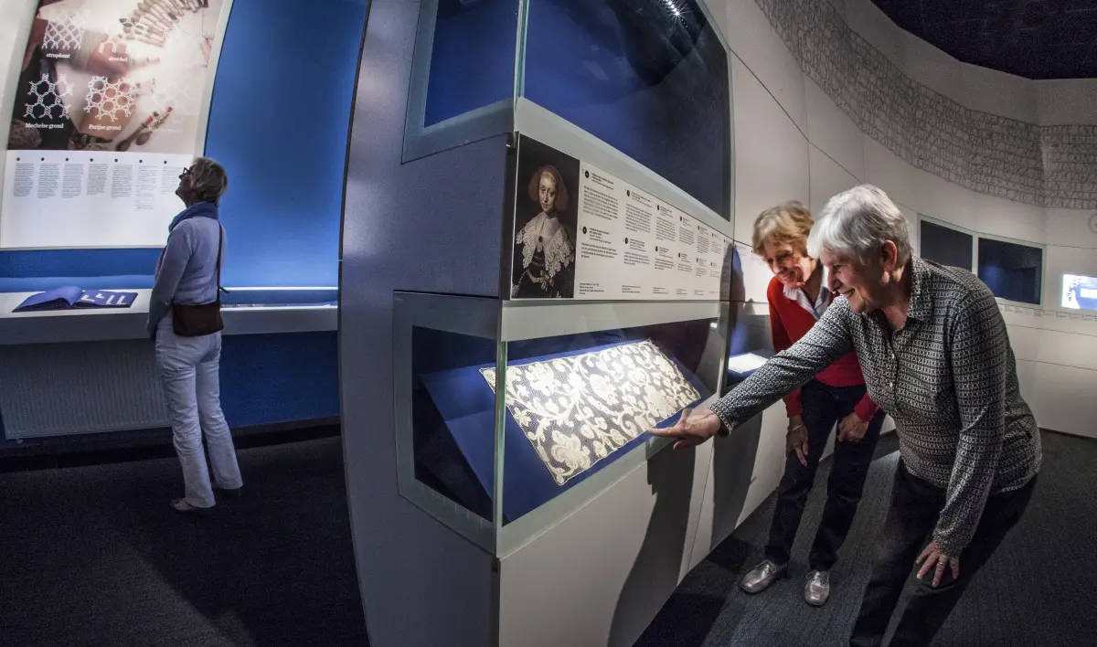 two visitors in front of a display case with a long lace cloth inside