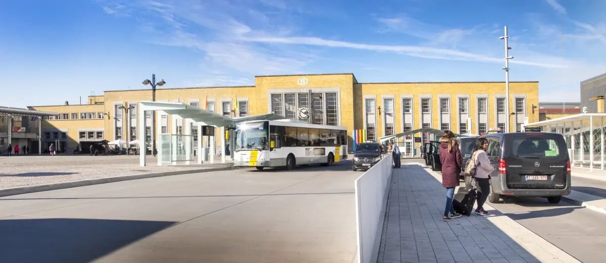 Station square with the front of the station. In front of the station, on the right, a row of taxis and on the left, a De Lijn bus.